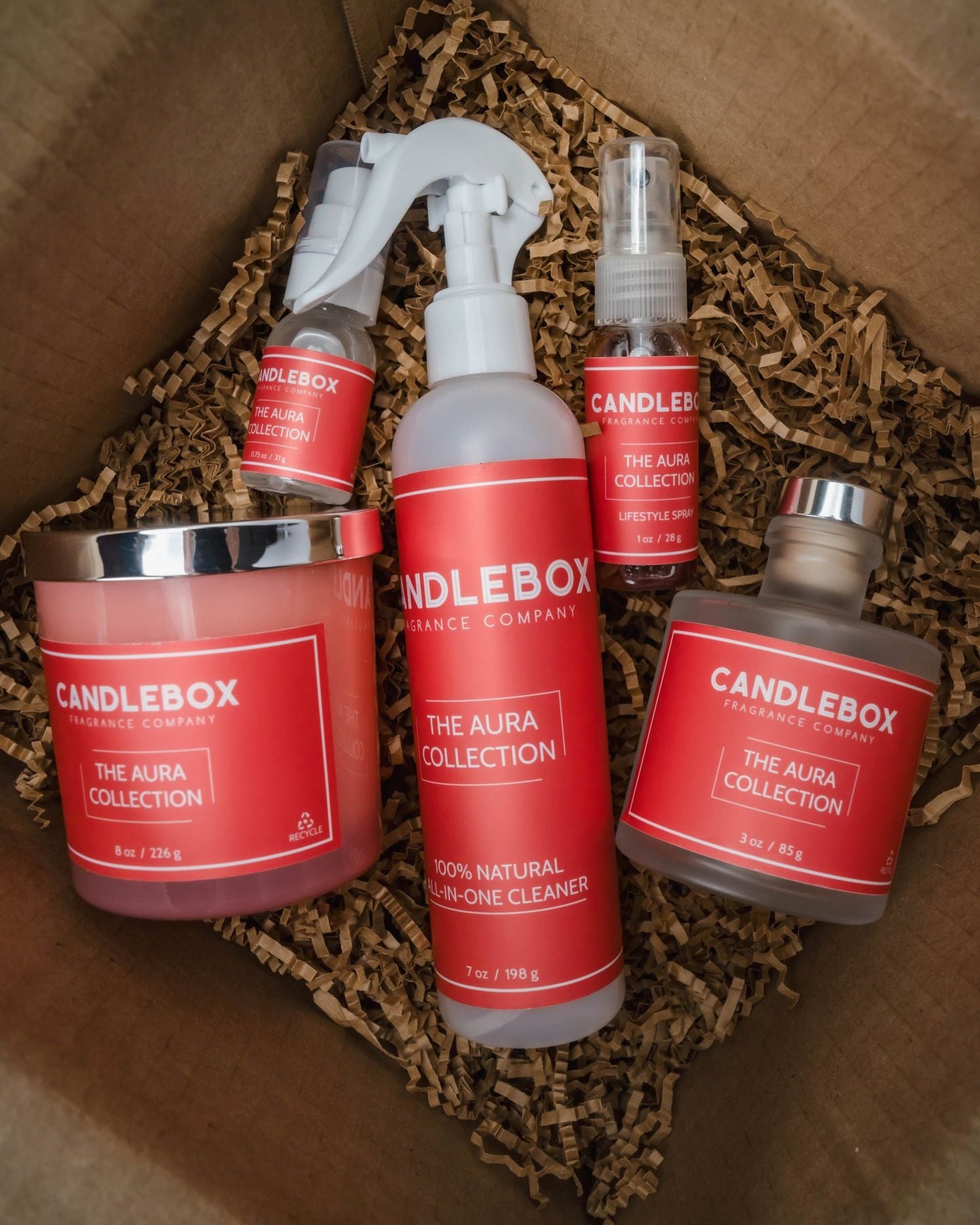 Monthly Candlebox set featuring The Aura Collection scented candles and cleaning products in a brown gift box with packing paper